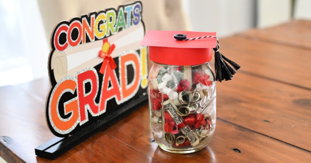 Jar filled with money next to congrats grad sign on table