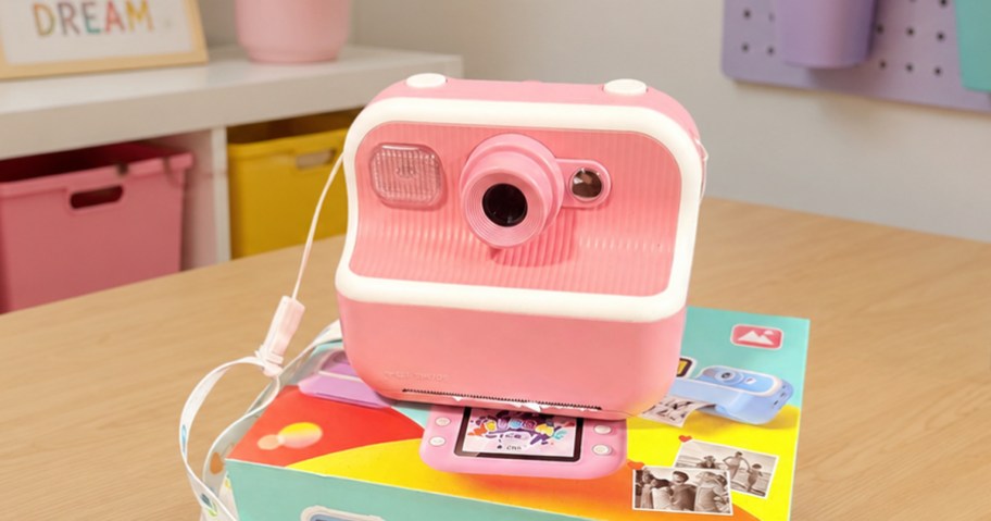Pink kids digital instant print camera sitting on a table in a playroom