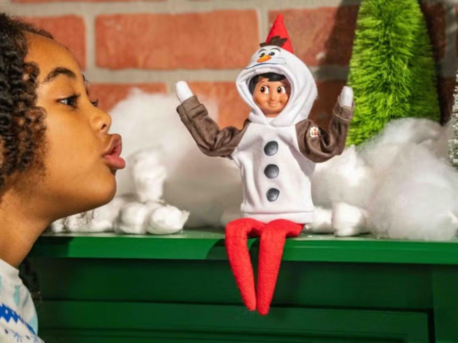 kid talking to Disney x Elf on the Shelf doll wearing olaf outfit on mantle