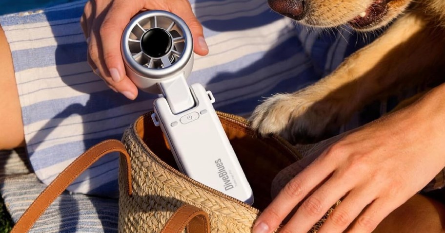 Hand holding white portable fan and placing it in handbag