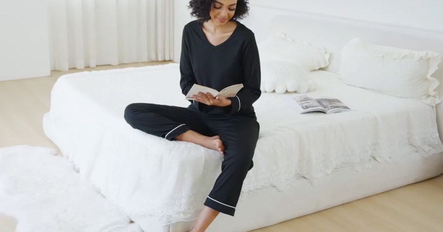 woman wearing pajamas and reading a book on a bed