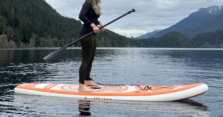 woman on an orange and white paddle board in lake