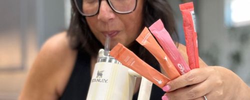 Hand holding 4 K2O hydration sticks in one hand while drinking from a Stanley tumbler