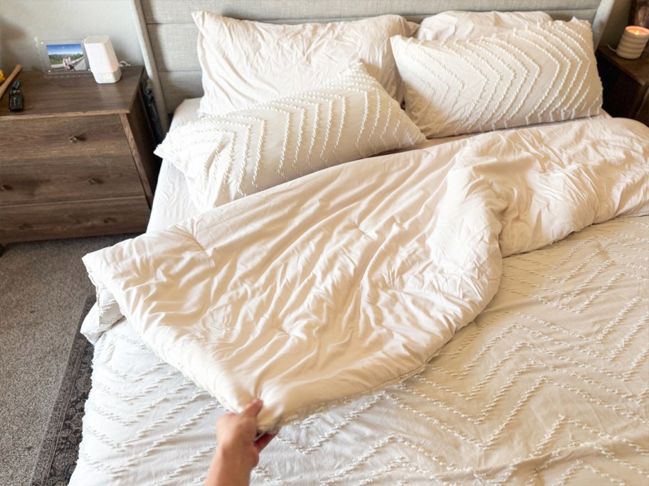 hand pulling back a white comforter on a bed