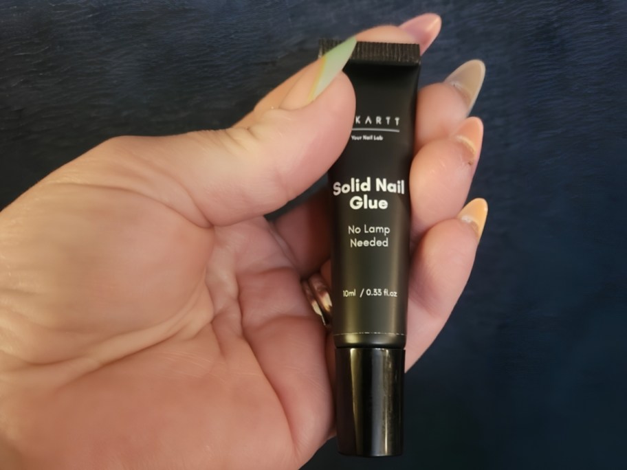 person holding markartt nail glue bottle with acrylic nails showing