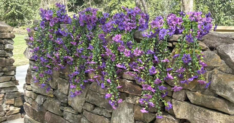 purple faux flowers draped over a rock wall
