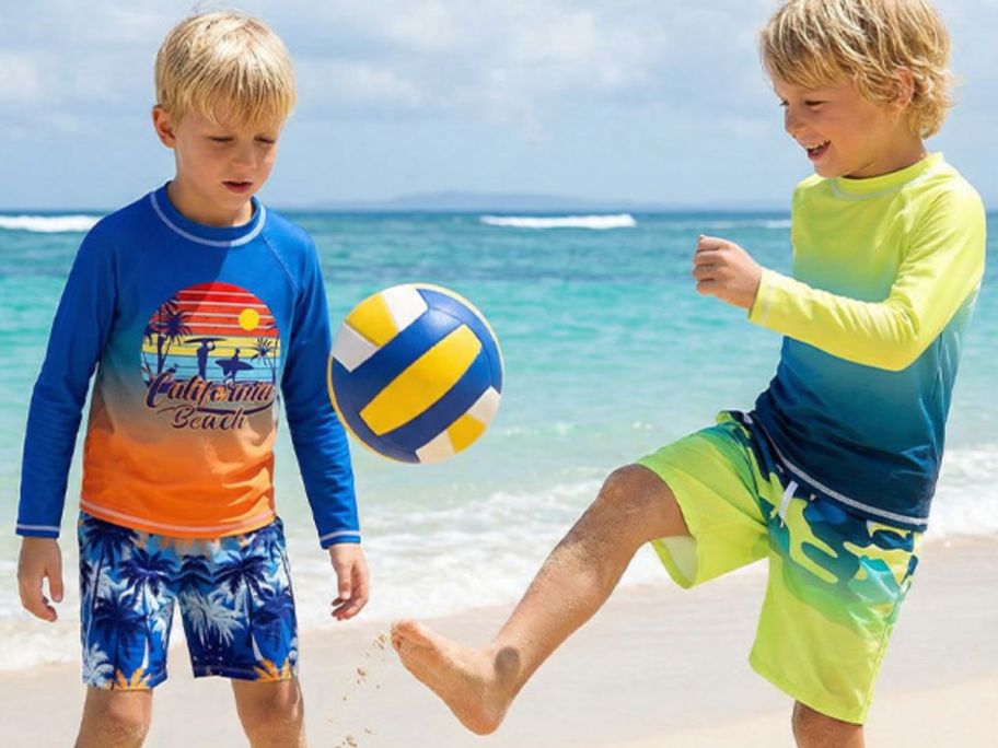 Two boys playing with a ball on a beach while wearing rashguard swim sets