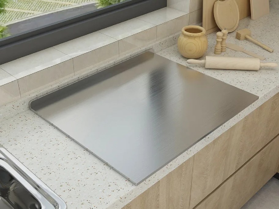 A polished stainless steel cutting board sits on a counter in a modern kitchen.