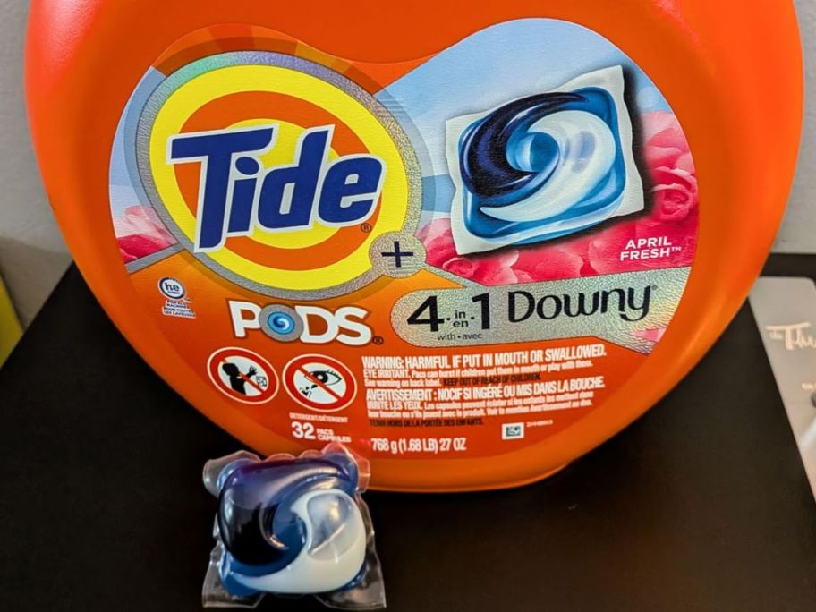 A Tub of Tide Pods with Downy with one pod placed in front of it