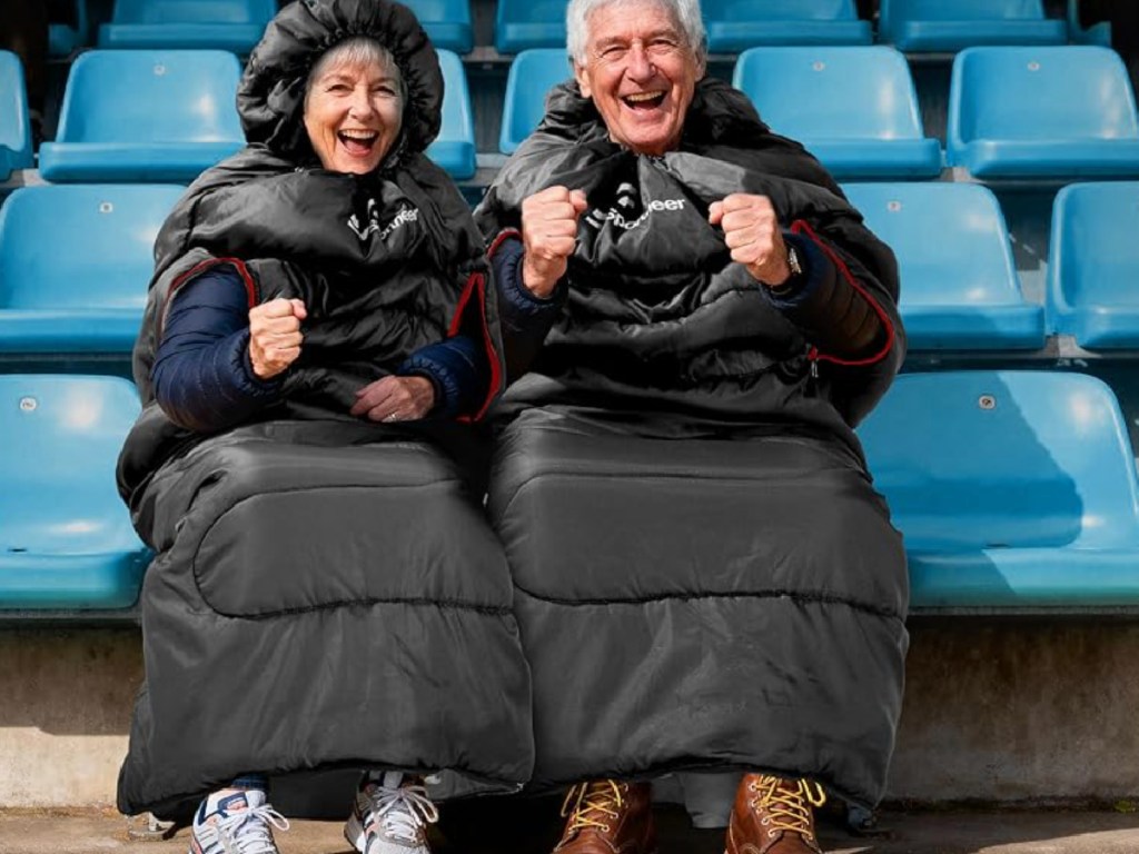 Man and woman wearing black, sleeping bags and sitting in stadium