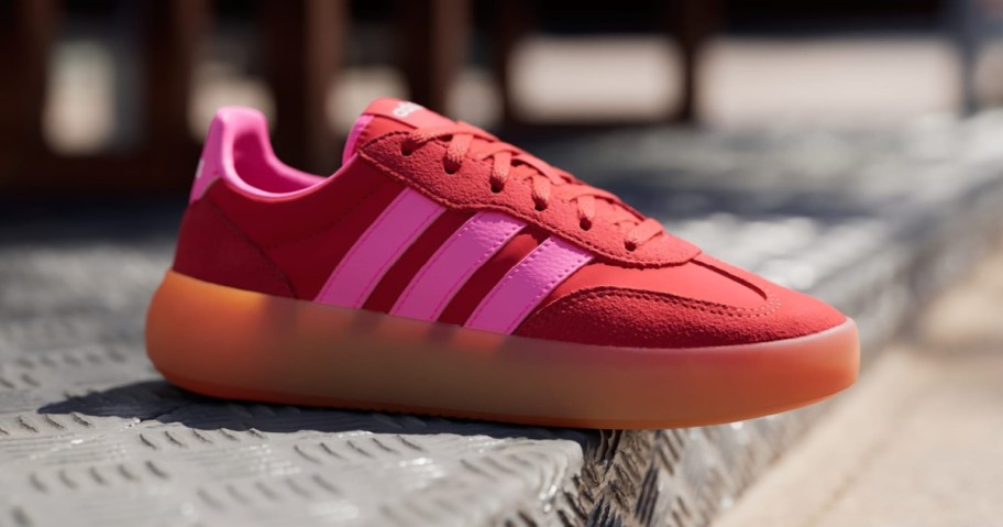A red sneaker with pink accents and three stripes on the side.