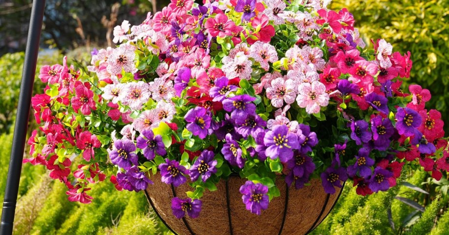 A vibrant hanging basket overflows with pink, purple, and white flowers in full bloom, set against lush green foliage.