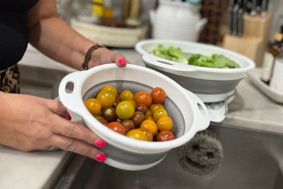 hands holding collander with tomatoes over sink