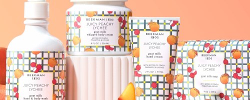 A collection of skincare products including a body wash, whipped body cream, hand cream, and soap all labeled "Juicy Peachy Lychee" by Beekman 1802. The packaging features a colorful geometric pattern with illustrations of peaches.