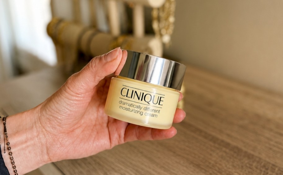 womans hand holding a jar of moisturizer