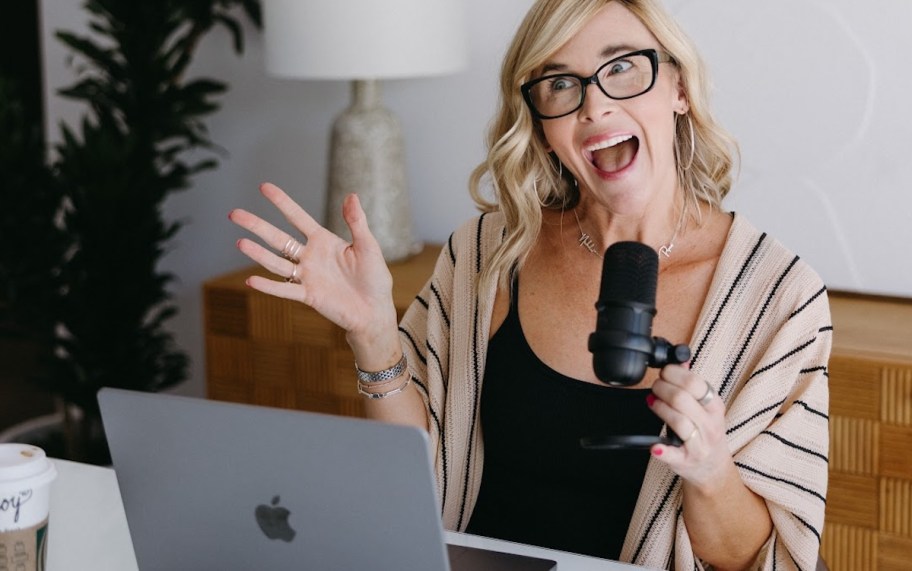 Woman holding microphone excitedly talking with laptop in front of her 