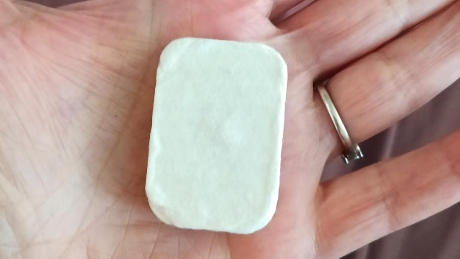 a womans hand holding a compressed face towel