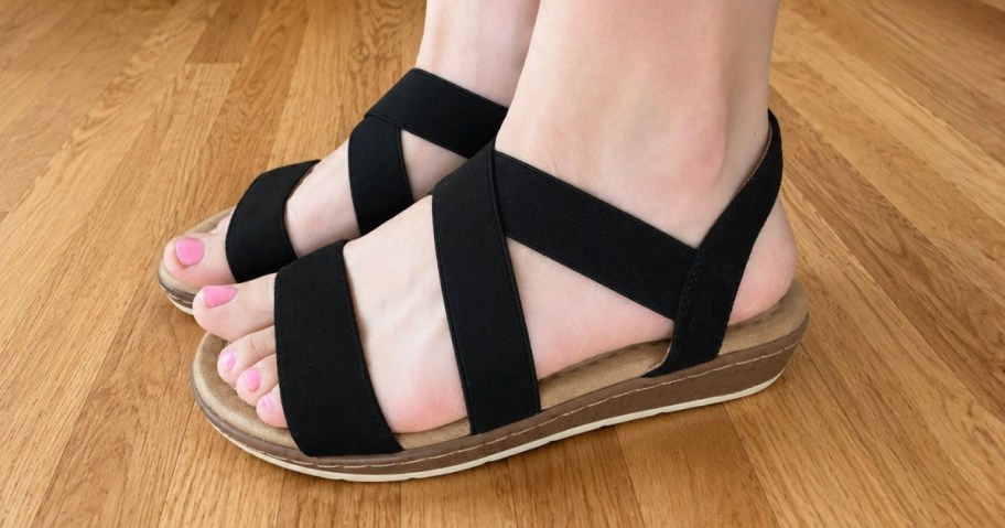 a woman's feet wearing low wedge sandals with black straps