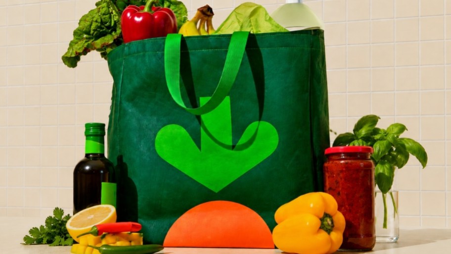 a green shopping bag filled with and surrounded by fresh produce