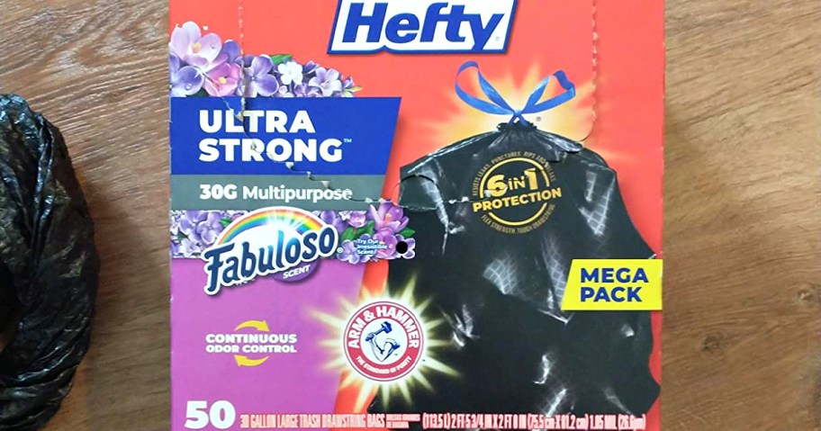 A box of Hefty Ultra Strong 30-gallon multipurpose trash bags with Fabuloso scent resting on a wooden floor.