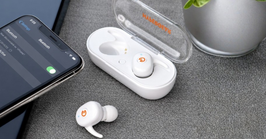a pair of earbuds with the charging case next to a smartphone