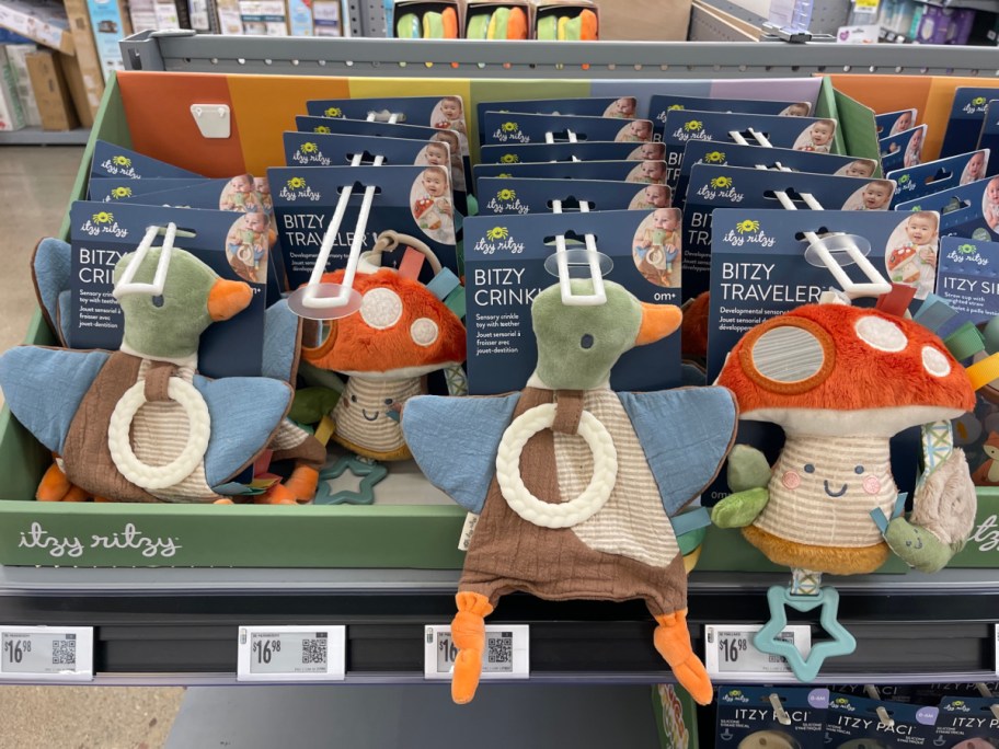 Itzy Ritzy plush duck and mushroom baby toys with teethers displayed in a store bin.