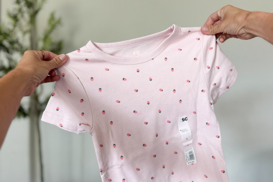 womans hands holding a pink baby tee