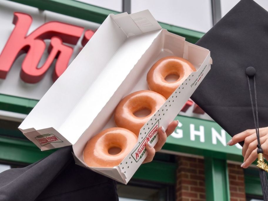 person holding krispy kreme grad 3 pack in front of store