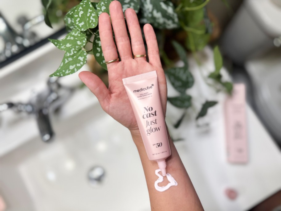 pink bottle of medicube No Cast Just Glow Collagen Sunscreen on woman's arm