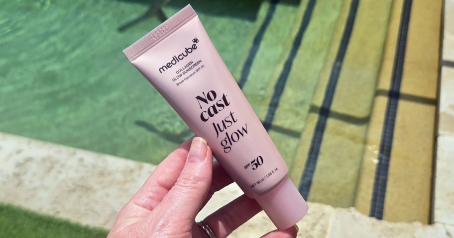 hand holding a tube of medicube No Cast Just Glow Collagen Sunscreen near pool