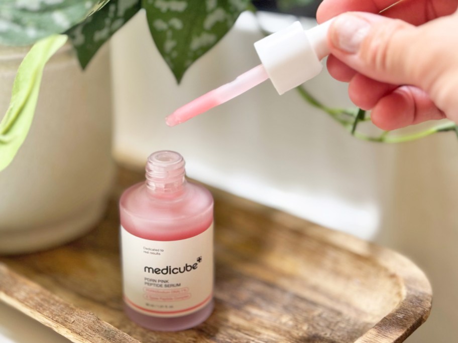 hand holding dropper to medicube PDRN Pink Peptide Serum bottle
