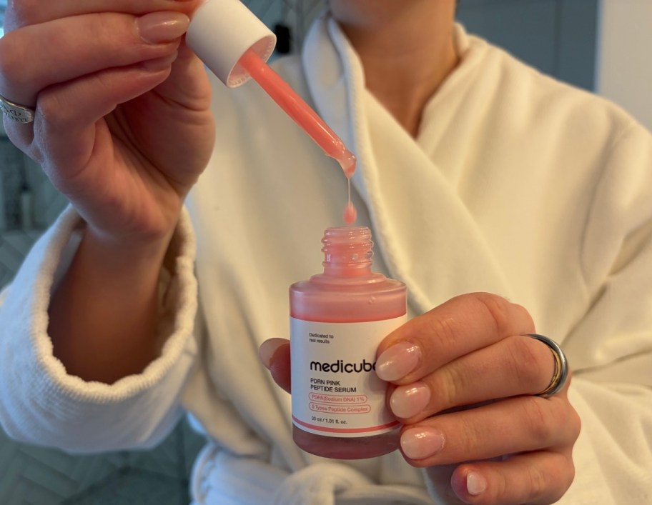 woman holding a bottle of serum with one hand and a dropper with the other