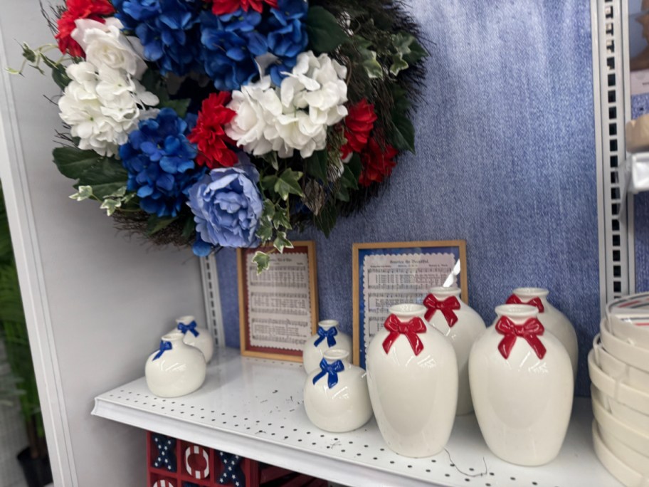 A shelf displays a patriotic-themed arrangement with a wreath of red, white, and blue flowers. Nearby, white vases adorned with red and blue bows.