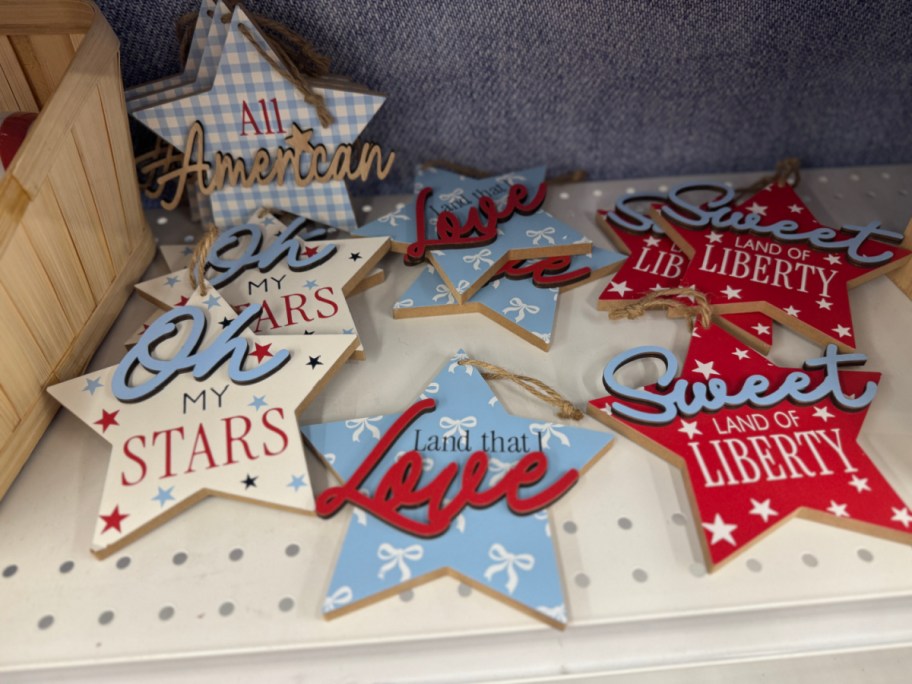 Wooden star-shaped ornaments display patriotic phrases in red, white, and blue.