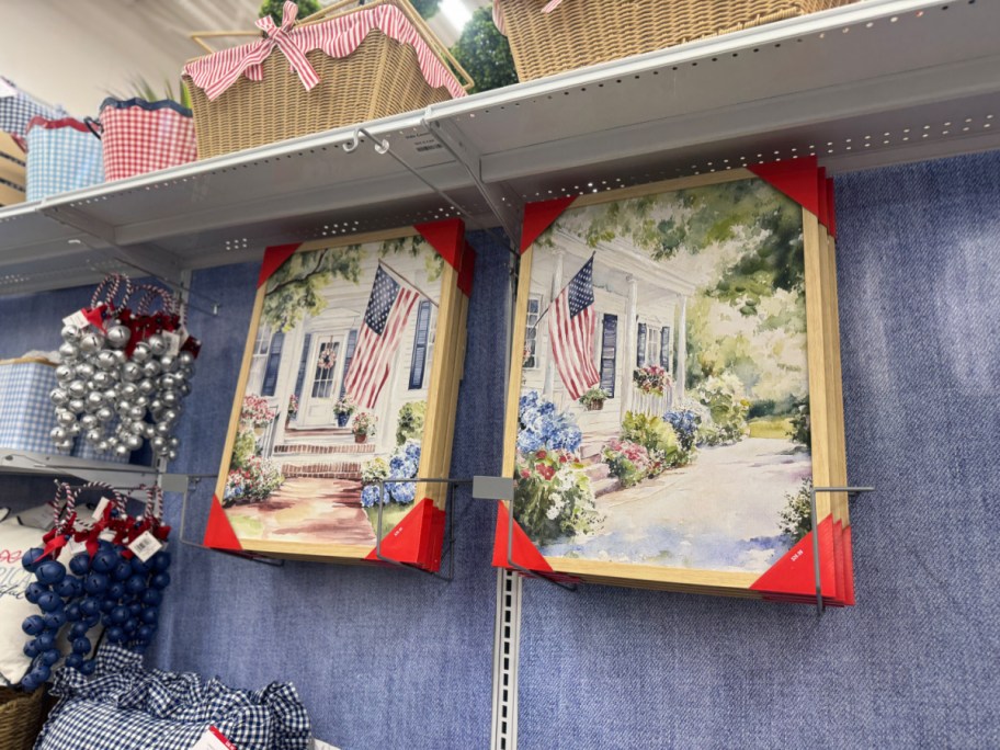 Paintings of American flags on a porch are displayed on shelves. 