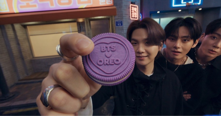 a boy holding up a purple OREO x BTS cookie