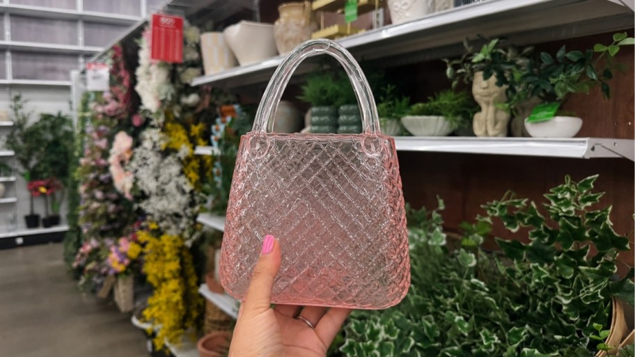 womans hand holding a pink glass purse shaped vase