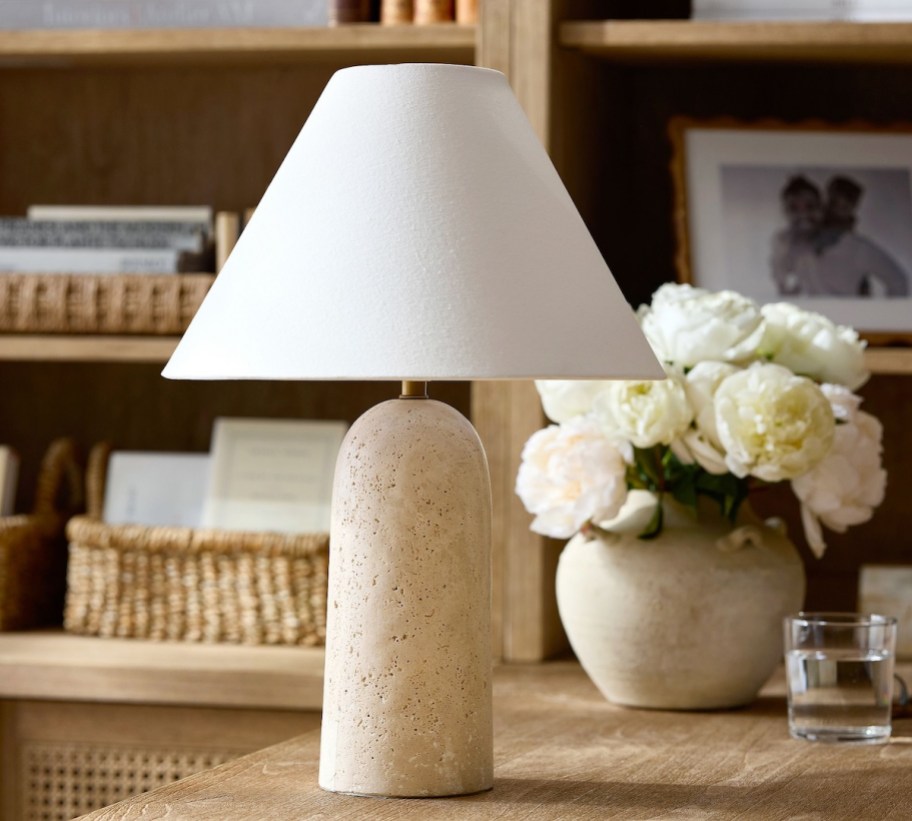 travertine table lamp with white shade on desk next to white flowers