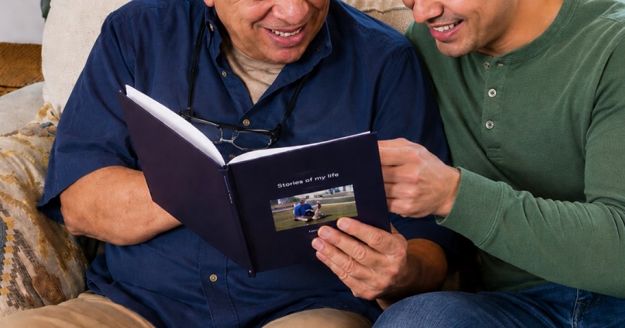 and older father and adult son looking at a memory book