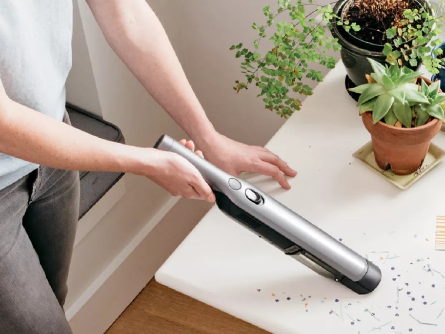 A person uses a sleek handheld vacuum to clean confetti off a table.
