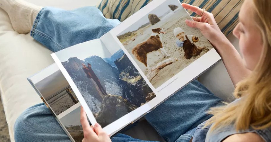 A person sitting on a couch, holding an open photo book with images of landscapes and animals.