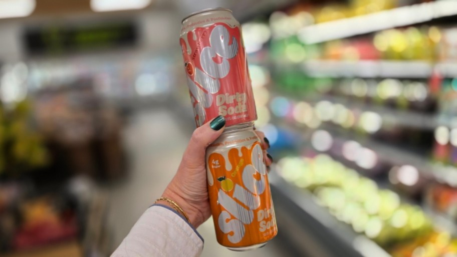 a womans hand holding 2 cans of slice dirty sodas
