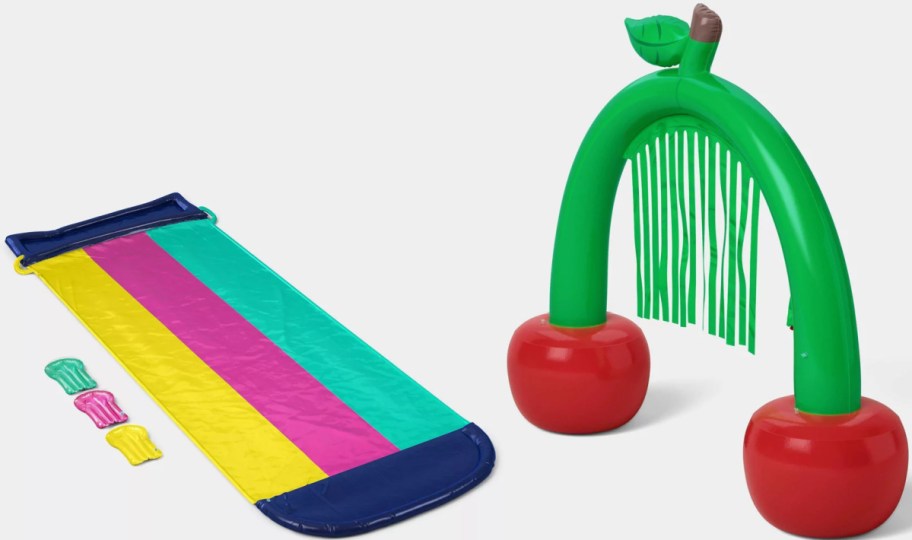 A colorful waterslide with a striped design next to an inflatable pool toy arch shaped like a fruit tree with two red cherries and green leaves.