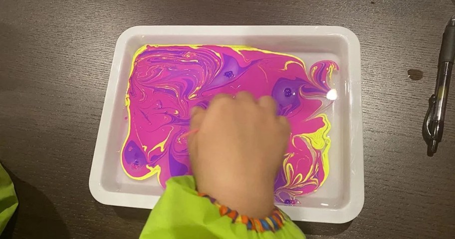 child's hand marbling paint in tray