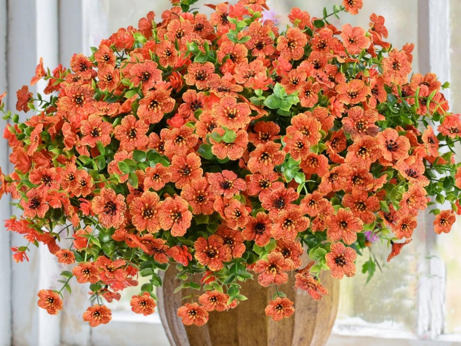 A large bouquet of vibrant orange flowers in a wooden pot, with green leaves mixed in.