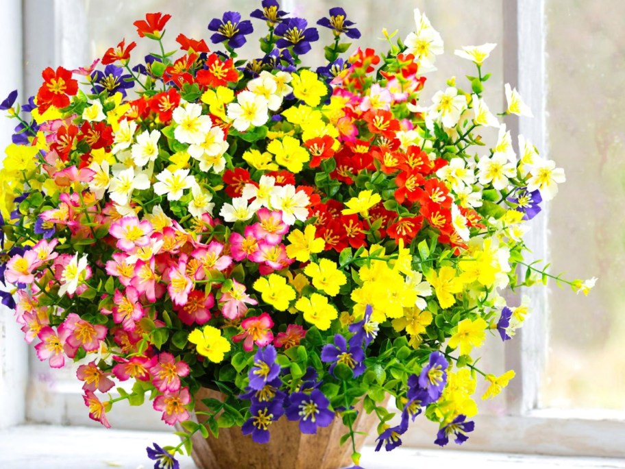 A vibrant bouquet of colorful artificial flowers in a pot, featuring shades of red, yellow, pink, white, and purple.
