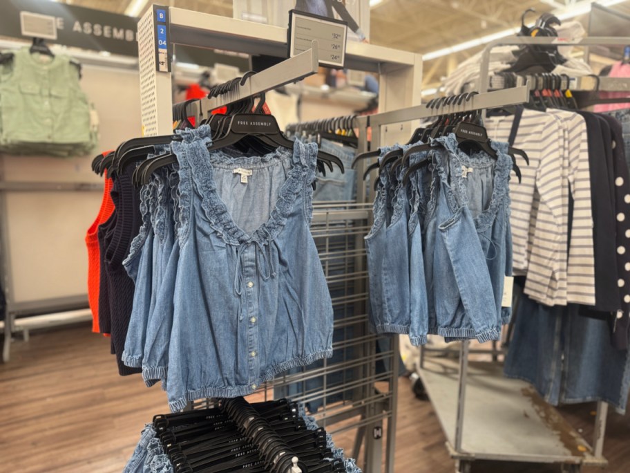 Racks of light blue denim tops with ruffled sleeves displayed in a store. The setting includes other clothing items like striped shirts and polka dots.
