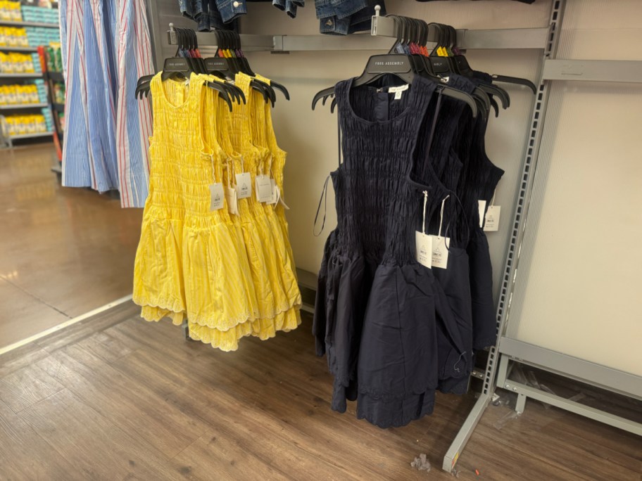 Displays of yellow and navy sundresses on hangers in a store aisle, with wooden floors and a nearby rack of striped garments.