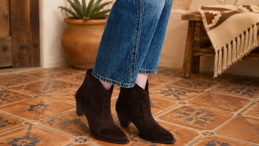 a womans feet wearing a pair of faux suede booties in dark brown