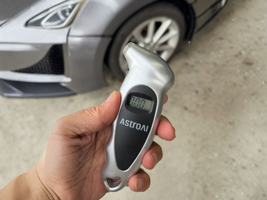 hand holding AstroAI Digital Tire Pressure Gauge in Silver in front of car tire